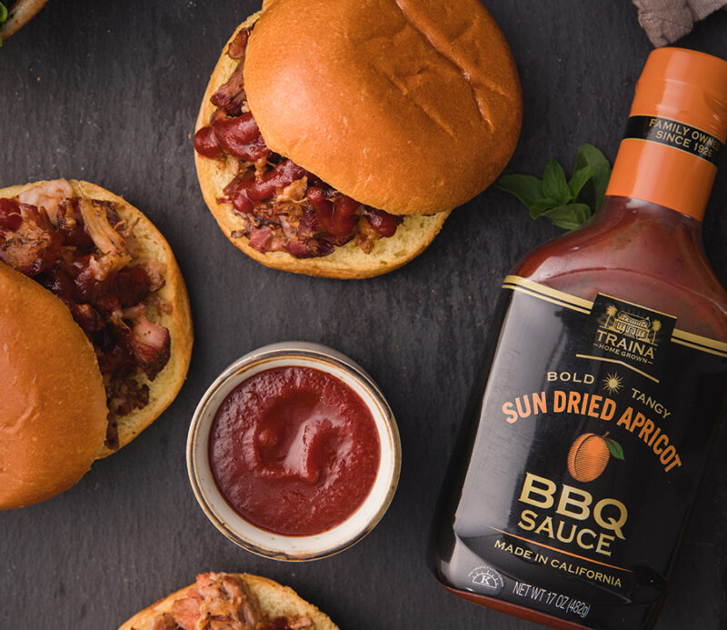 Overhead view of Sun Dried Apricot BBQ Sauce bottle next to pulled pork sandwiches.