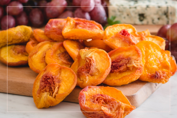 Close-up of moist, colorful sun-dried peaches in reddish-orange and yellow hues cascading on a wooden block, with fresh red grapes in the background. A vibrant, easy appetizer perfect for holidays and special events.